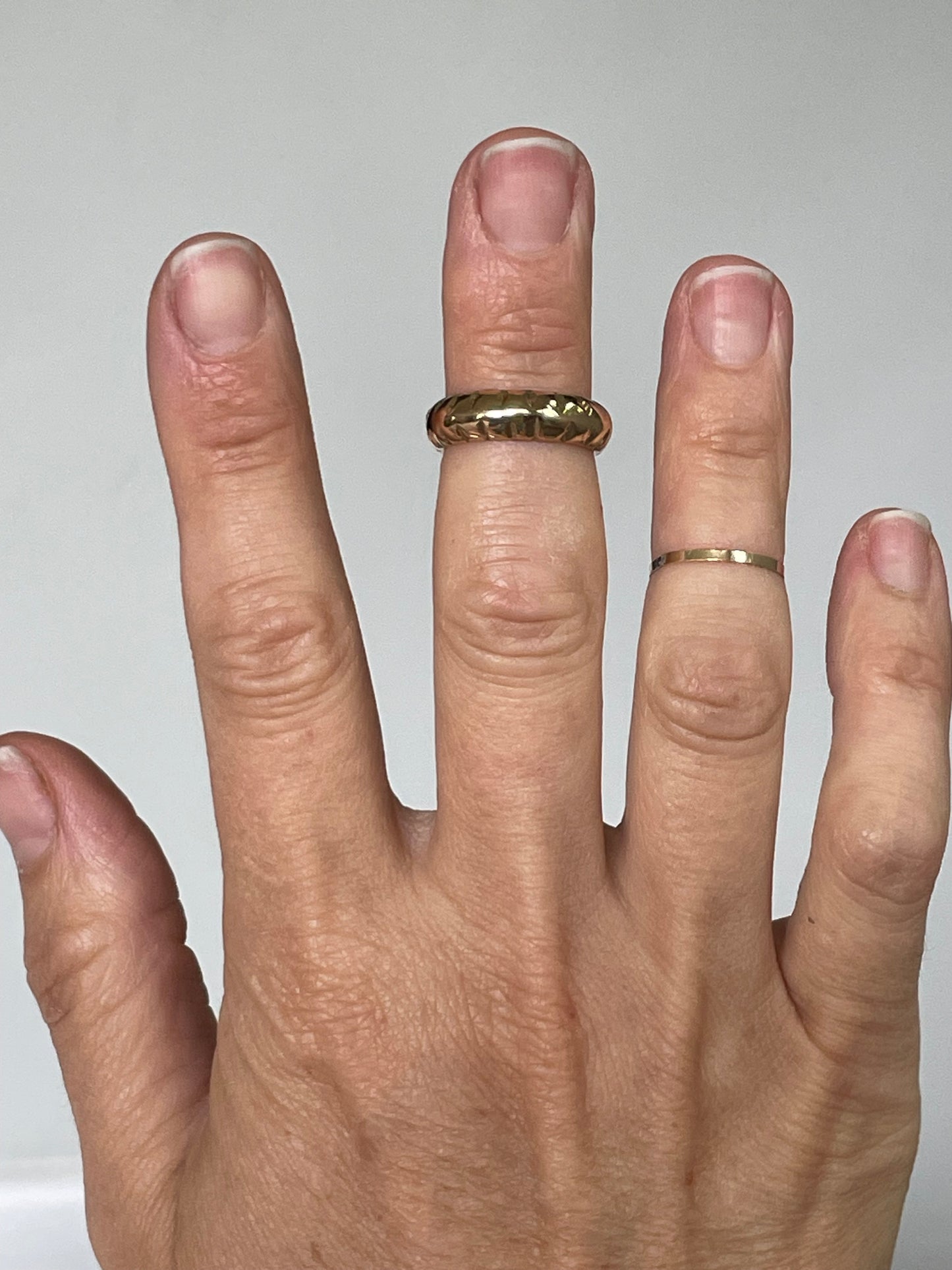 Hand wearing a gold ring on a plain background