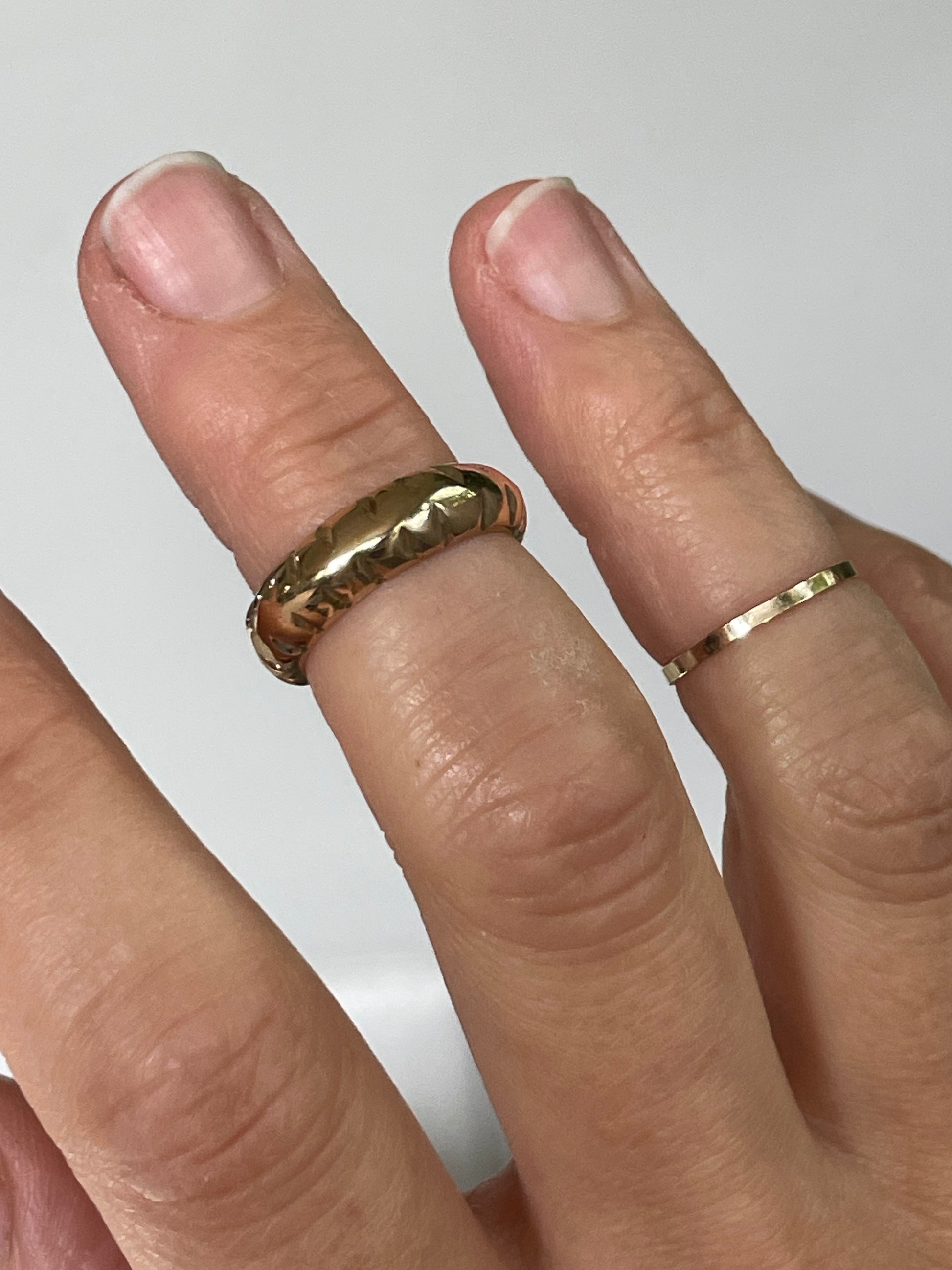 Hand wearing a gold ring on a plain background