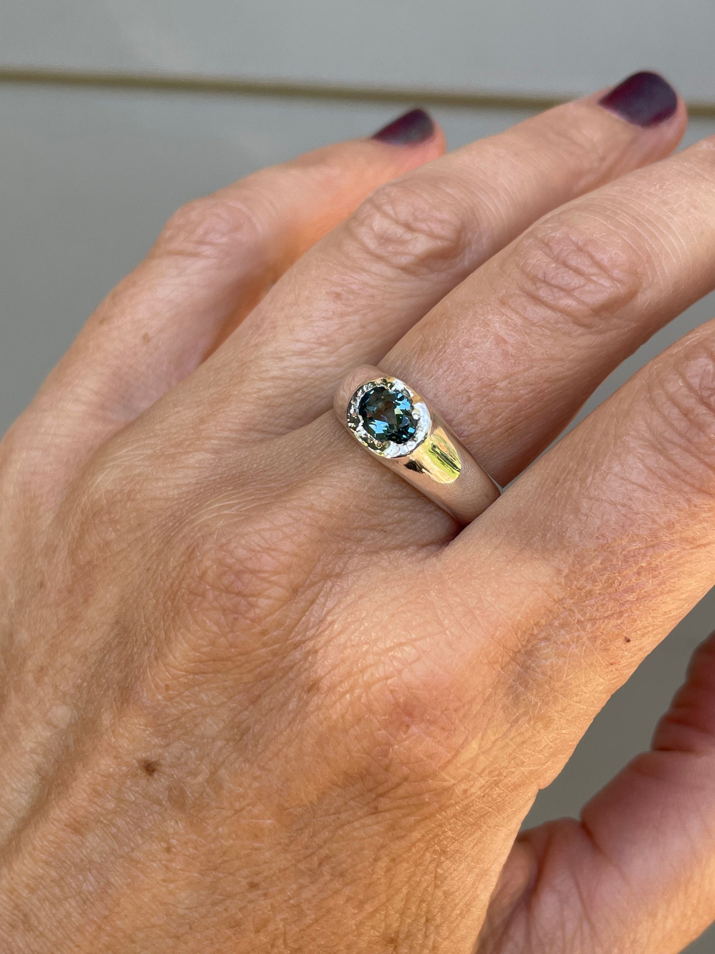 A close-up of a hand wearing a silver ring with a round blue gemstone in a bezel setting.